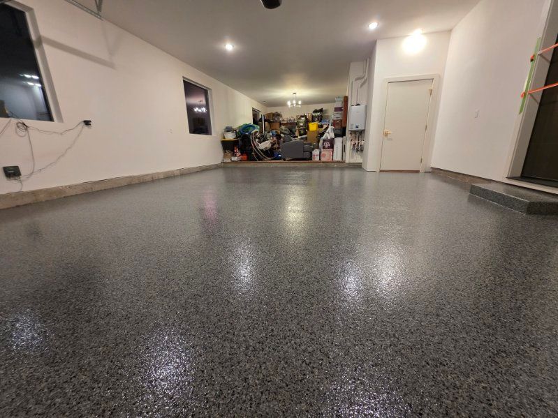 Garage with shiny, speckled gray floor; white walls; cluttered back area.