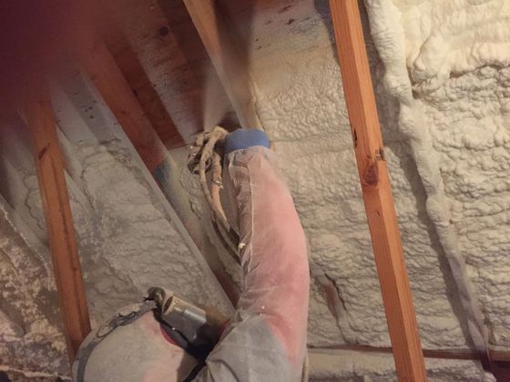 A man is spraying foam on the ceiling of a house.
