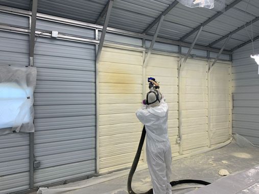 A man is spraying foam on a wall in a garage.