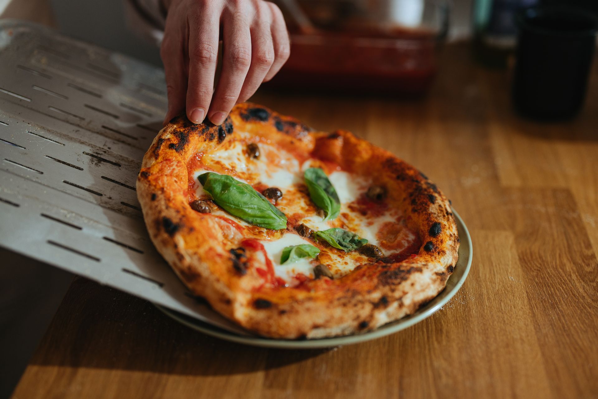 Una persona sta mettendo una pizza su un piatto su un tavolo di legno.