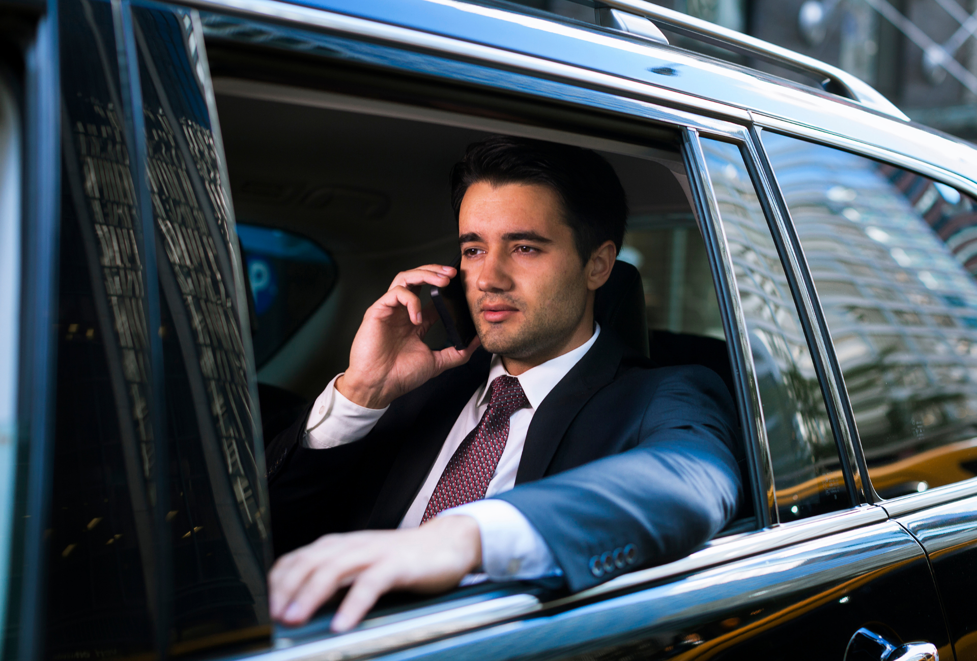 A man in a suit and tie is sitting in a car talking on a cell phone.