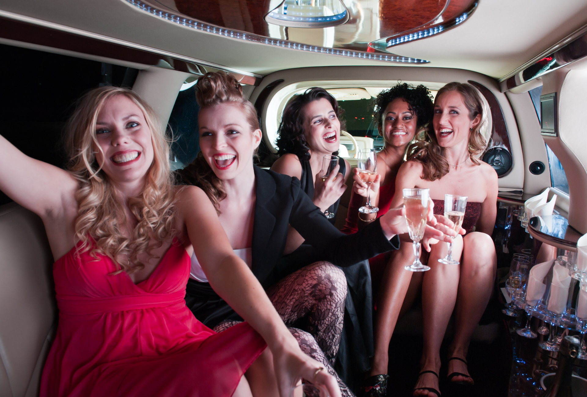 A group of women are sitting in a limousine holding champagne glasses.