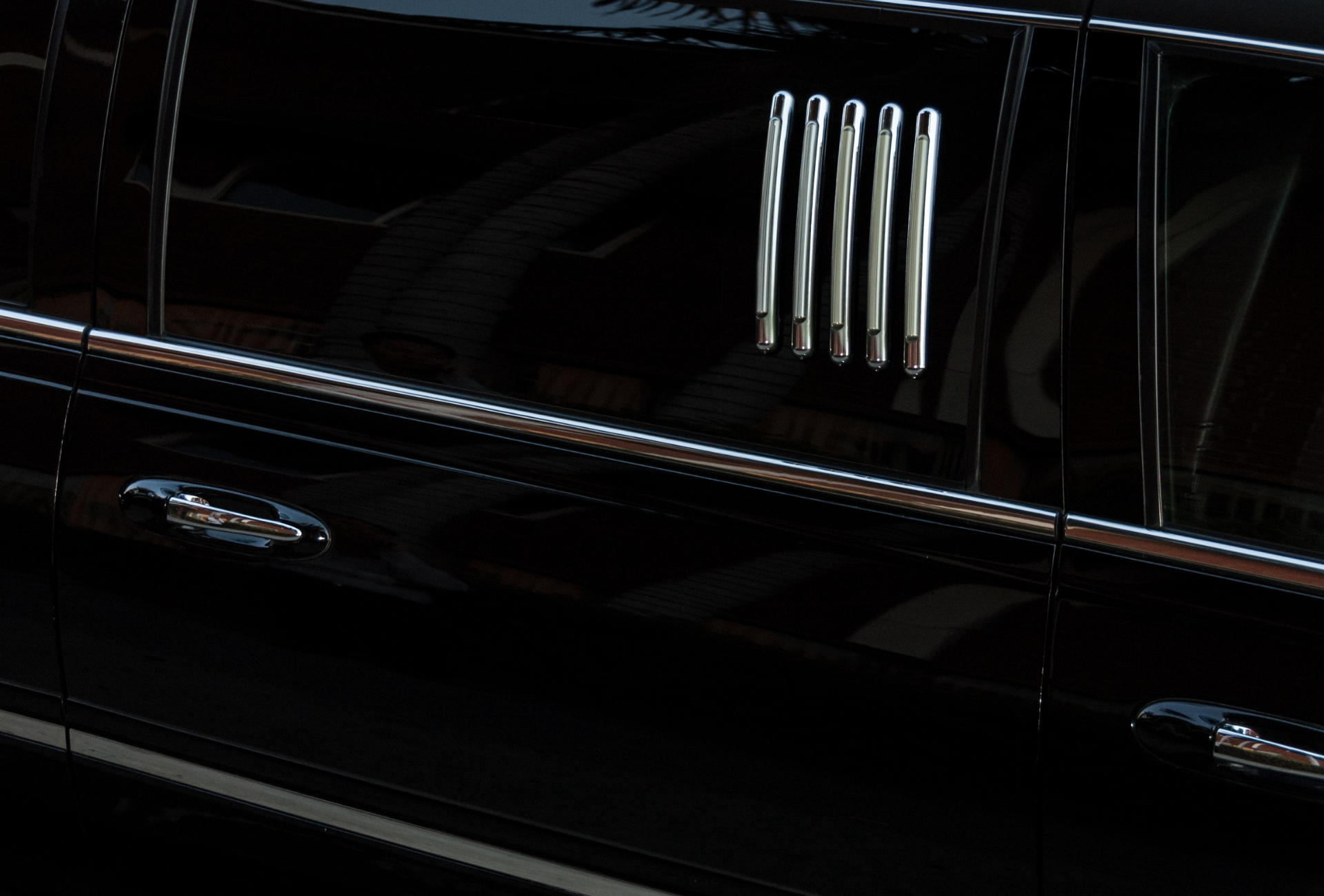 A close up of the side of a black limousine with chrome trim.