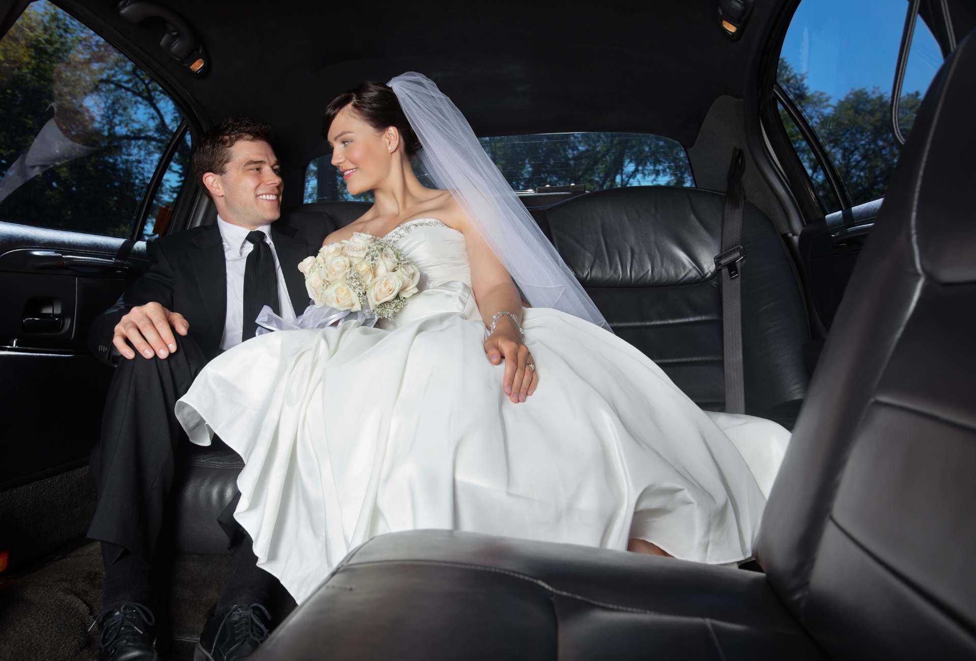 A bride and groom are sitting in the back seat of a limousine.