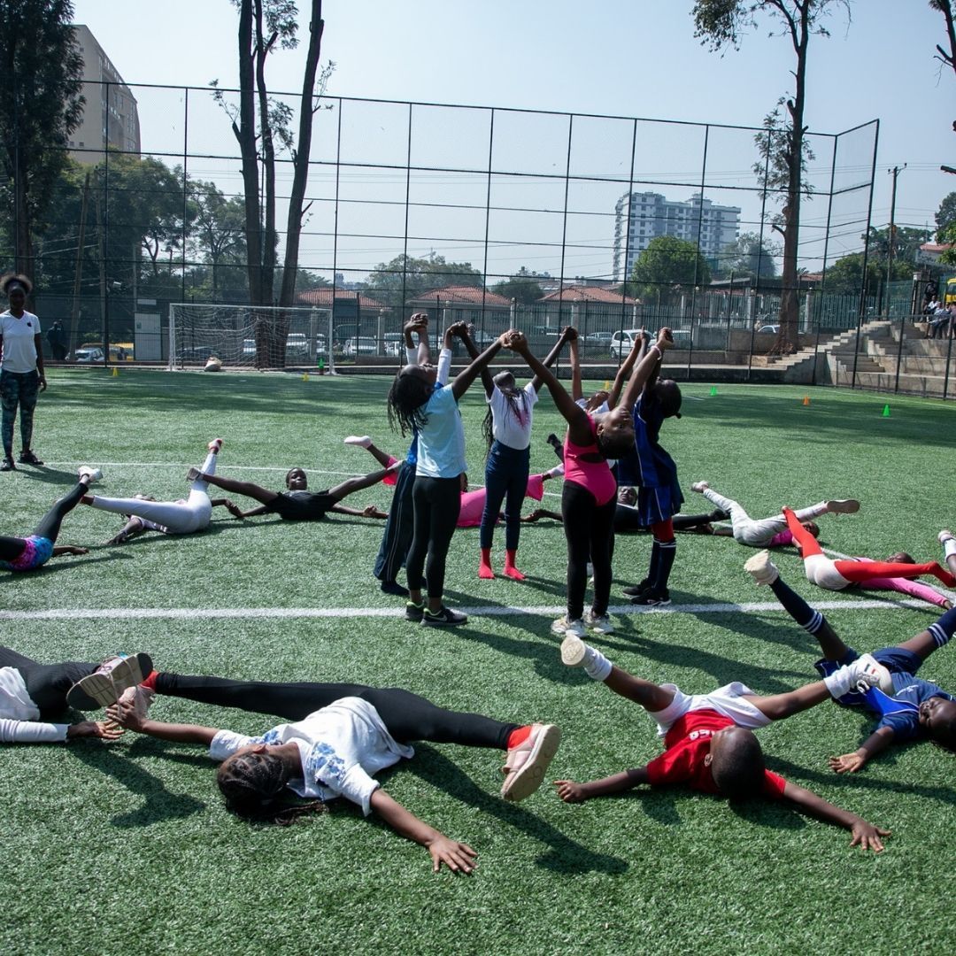 A group of children are doing stretching exercises on a soccer field.