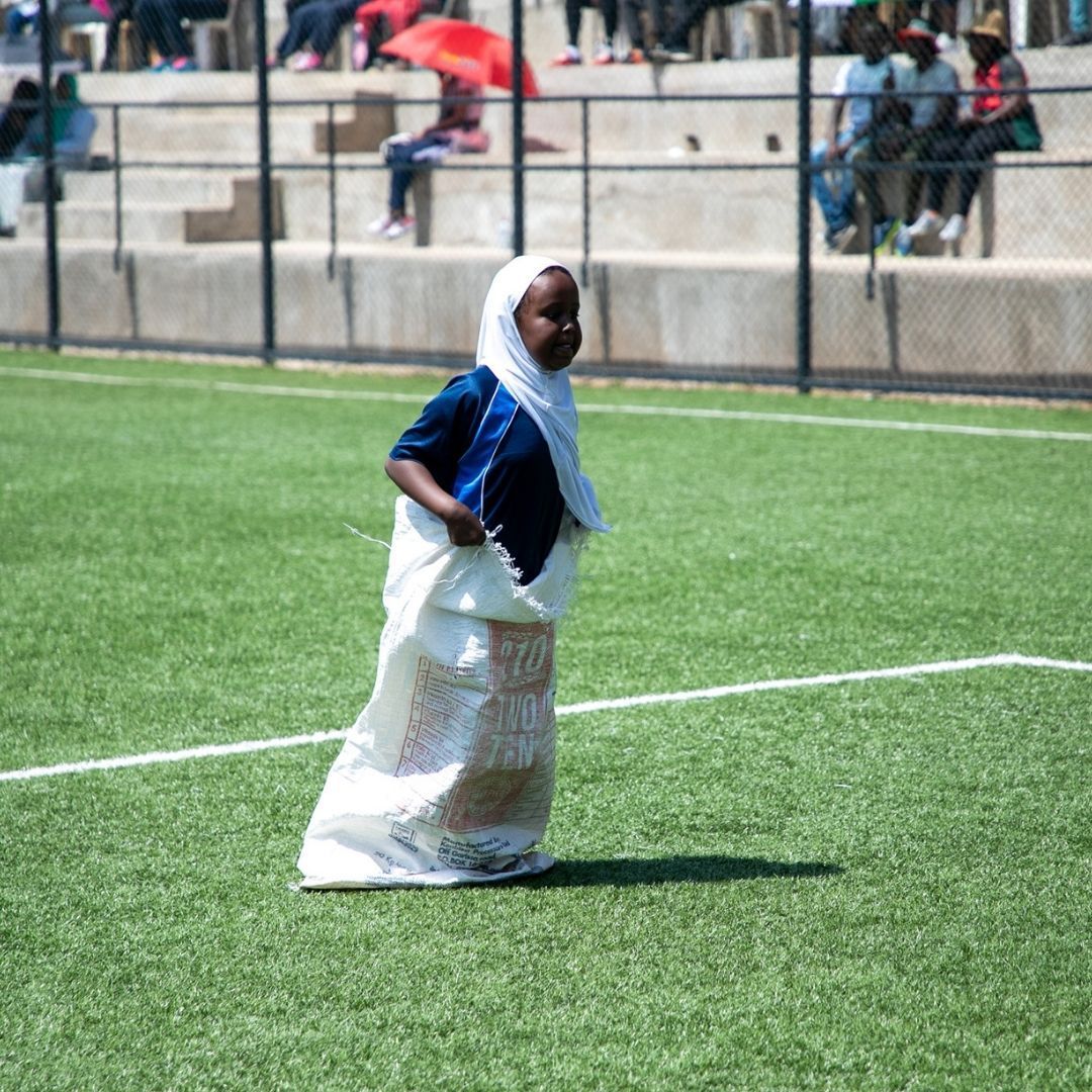 A girl wearing a hijab is running on a soccer field