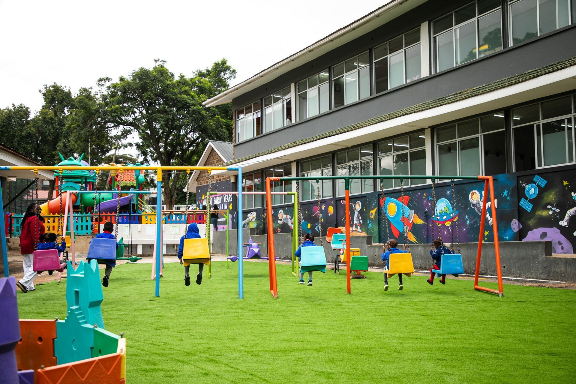 A playground with swings and a mural on the wall in front of a building.