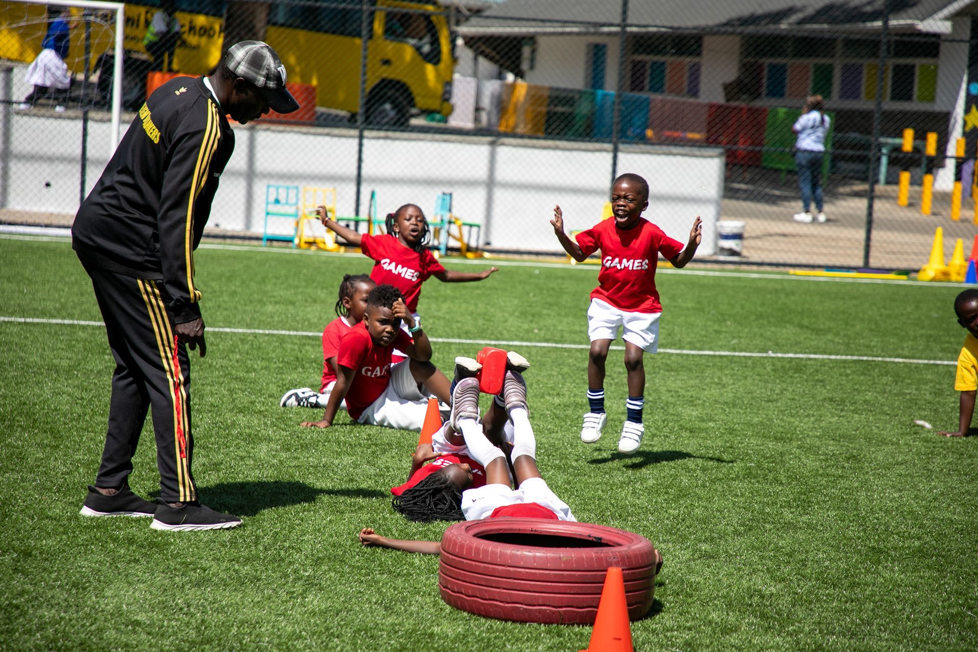 A man is standing next to a group of children on a soccer field.
