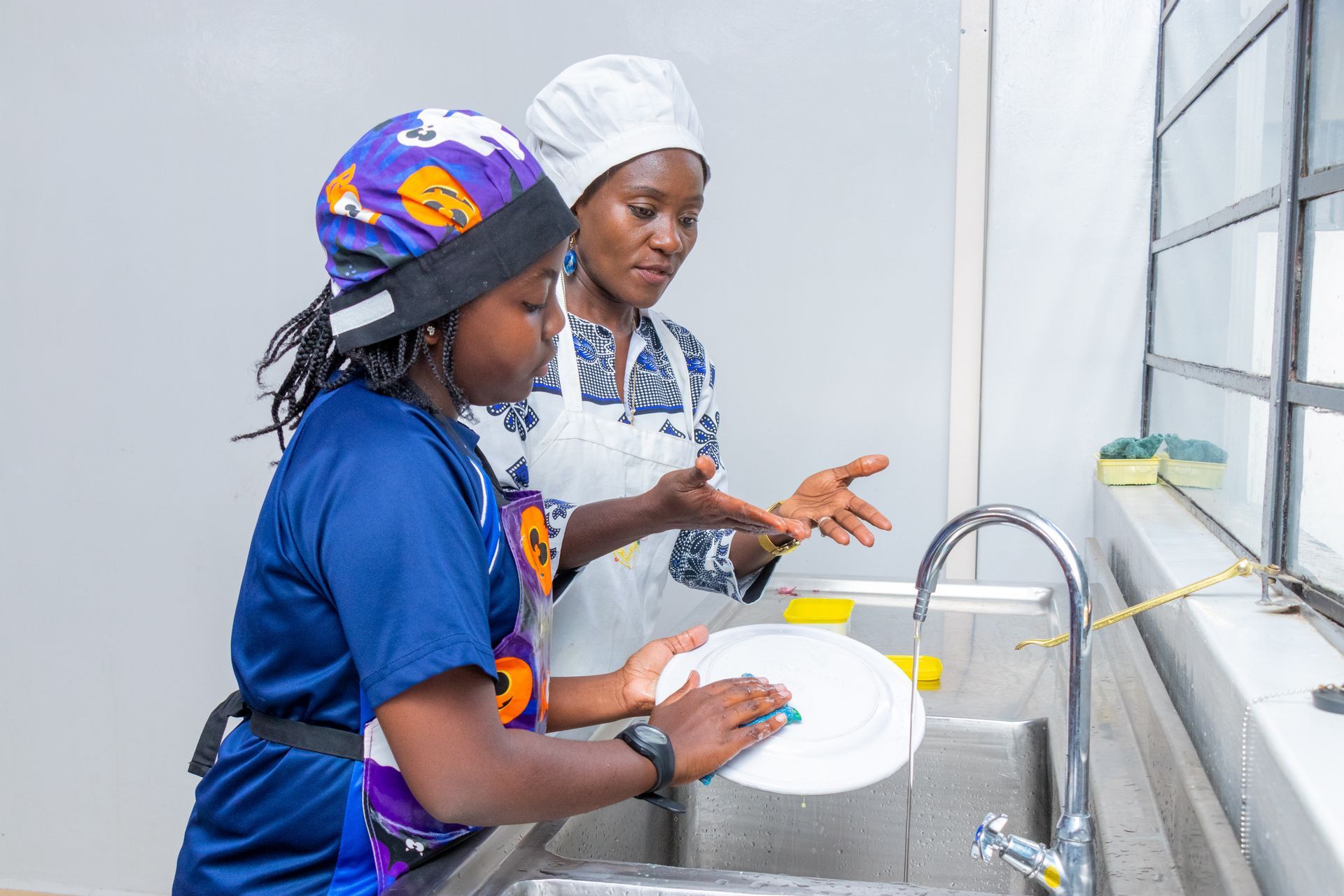 Two women are washing dishes in a kitchen sink.