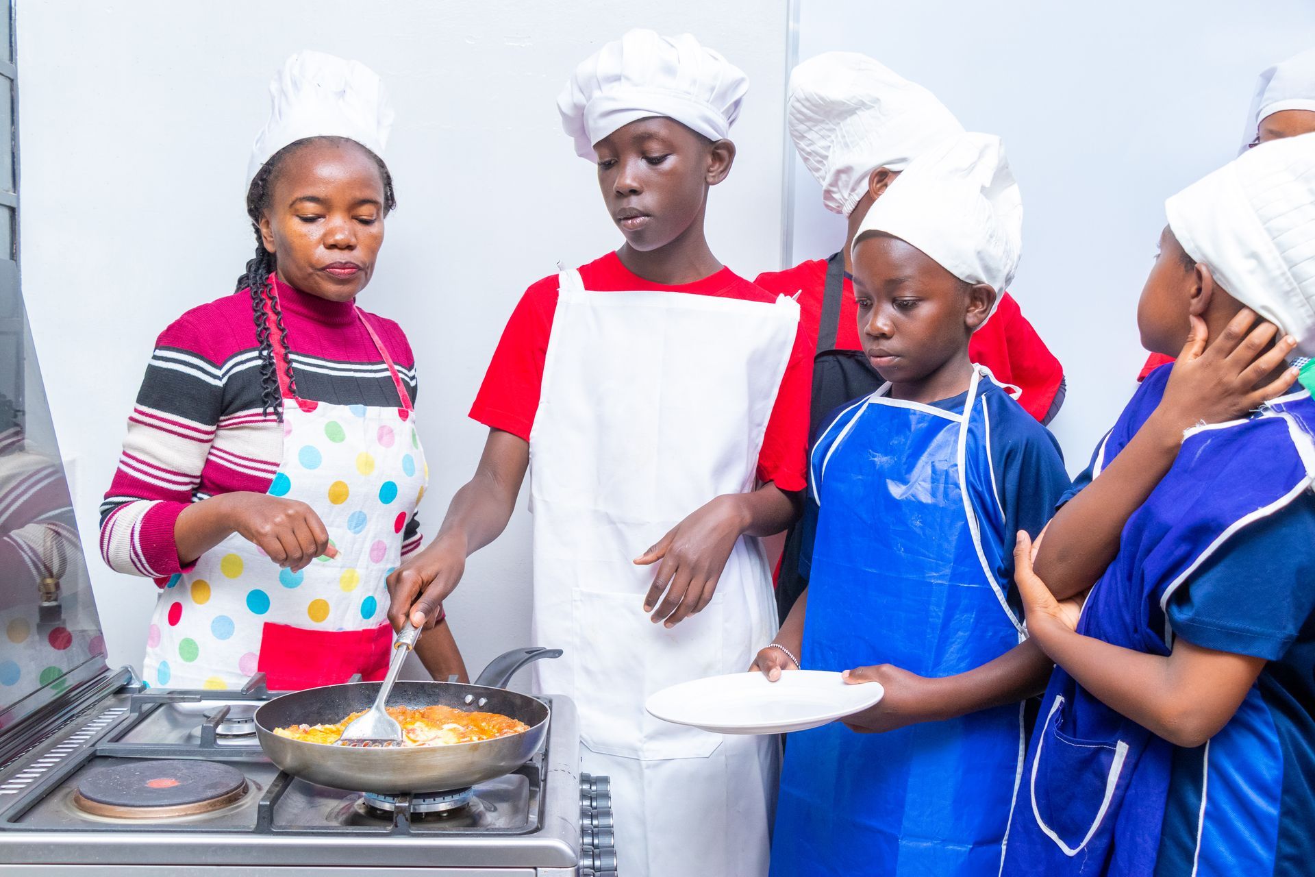 A group of children are standing around a stove cooking food.