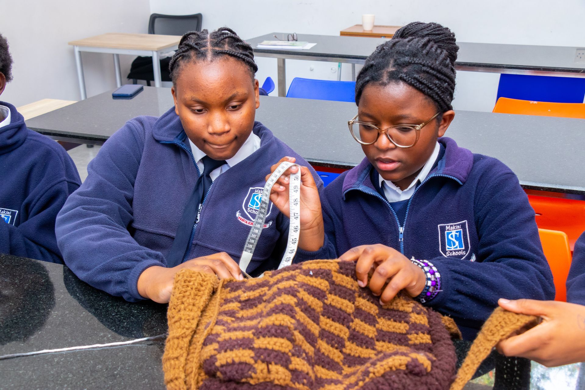 A group of young girls are sitting at a table measuring a piece of fabric.