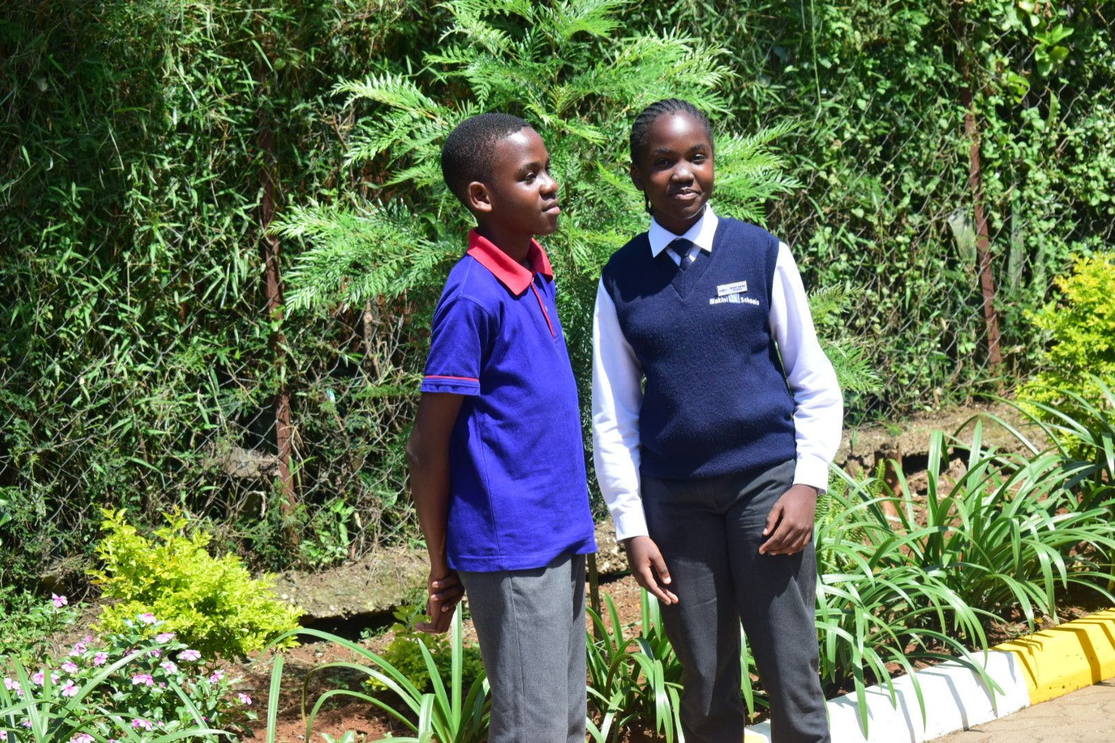 A boy and a girl are standing next to each other in a garden.