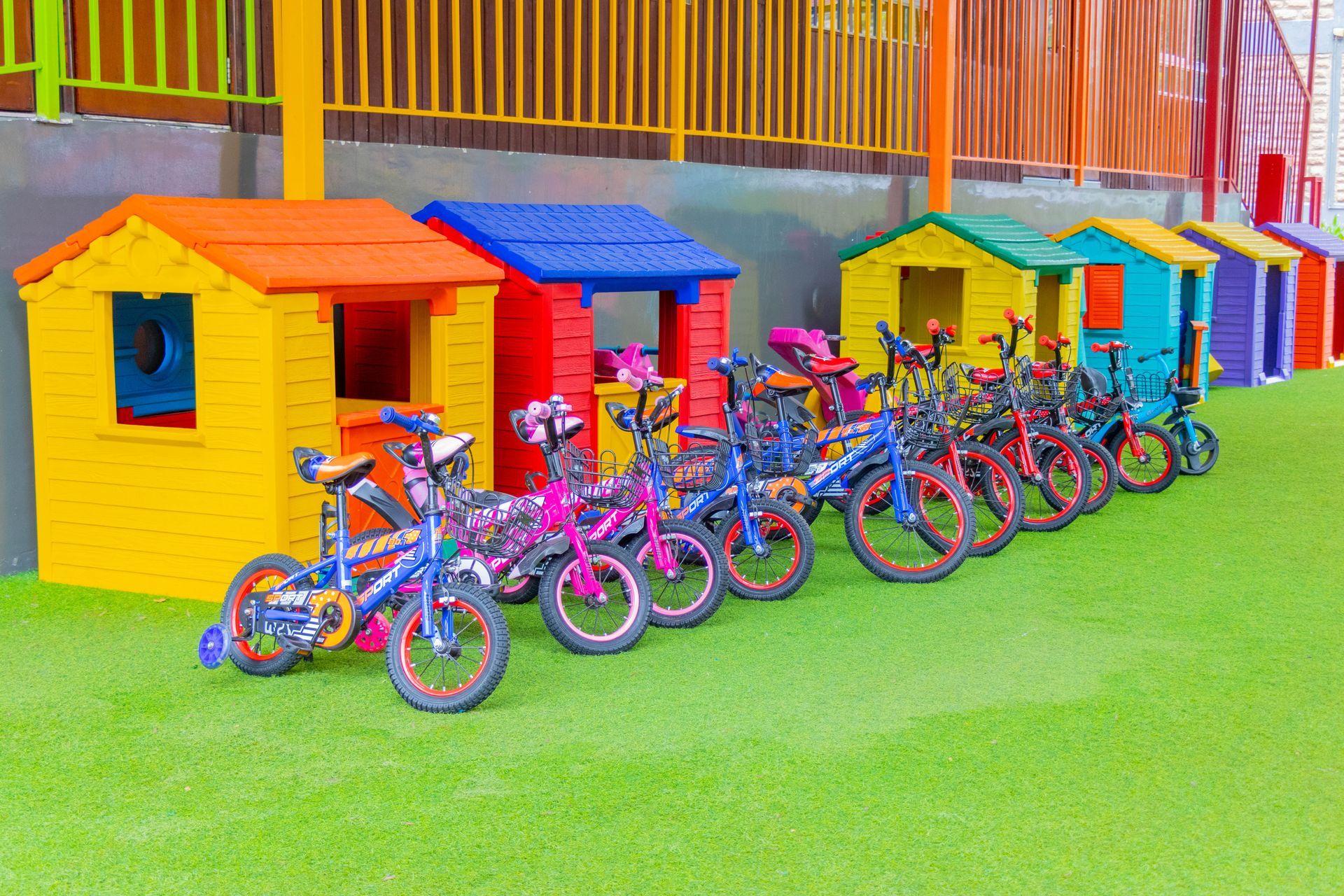 A row of bicycles are parked in front of colorful playhouses in a playground.