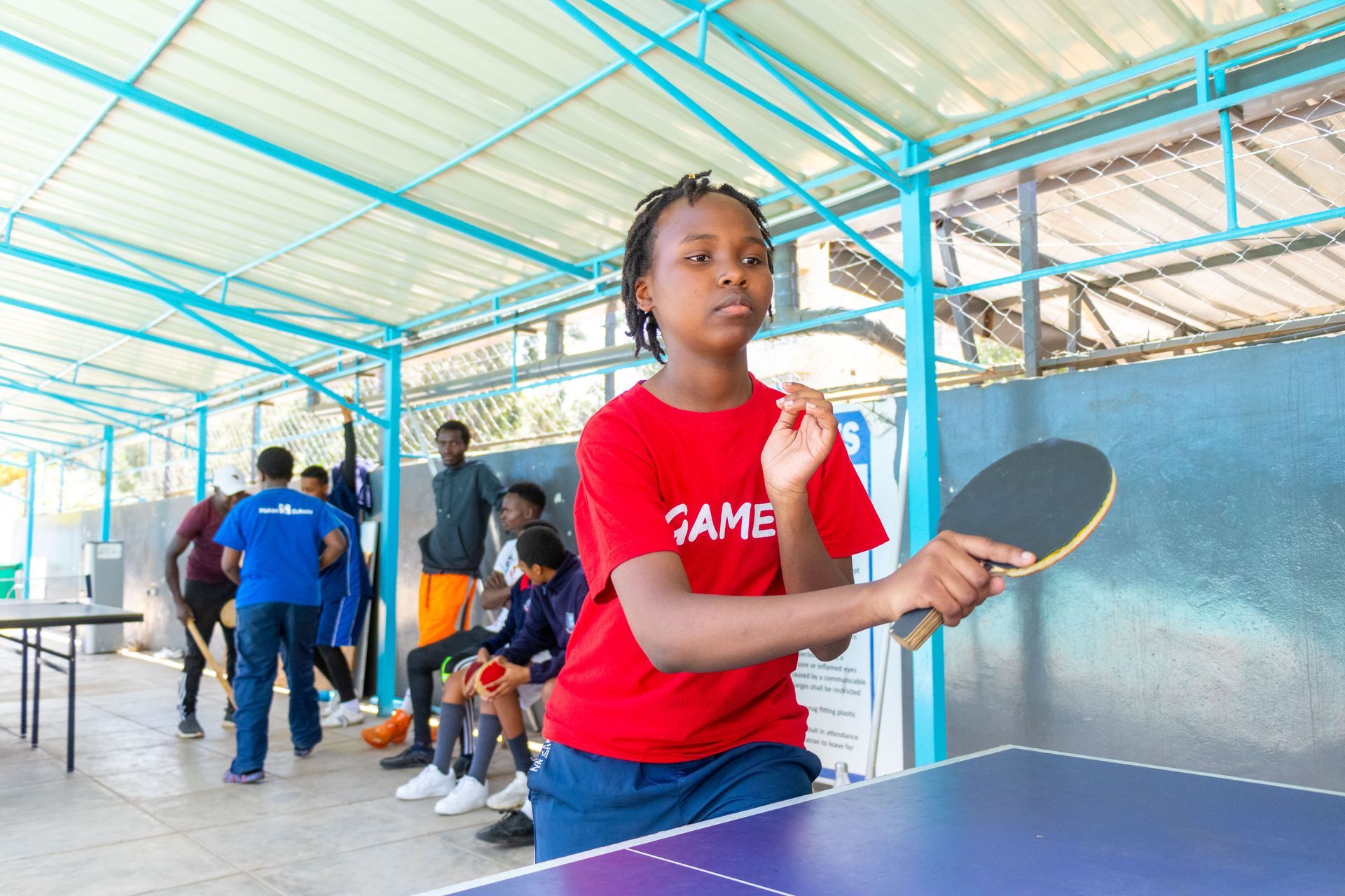 A girl in a red shirt is playing ping pong on a table.