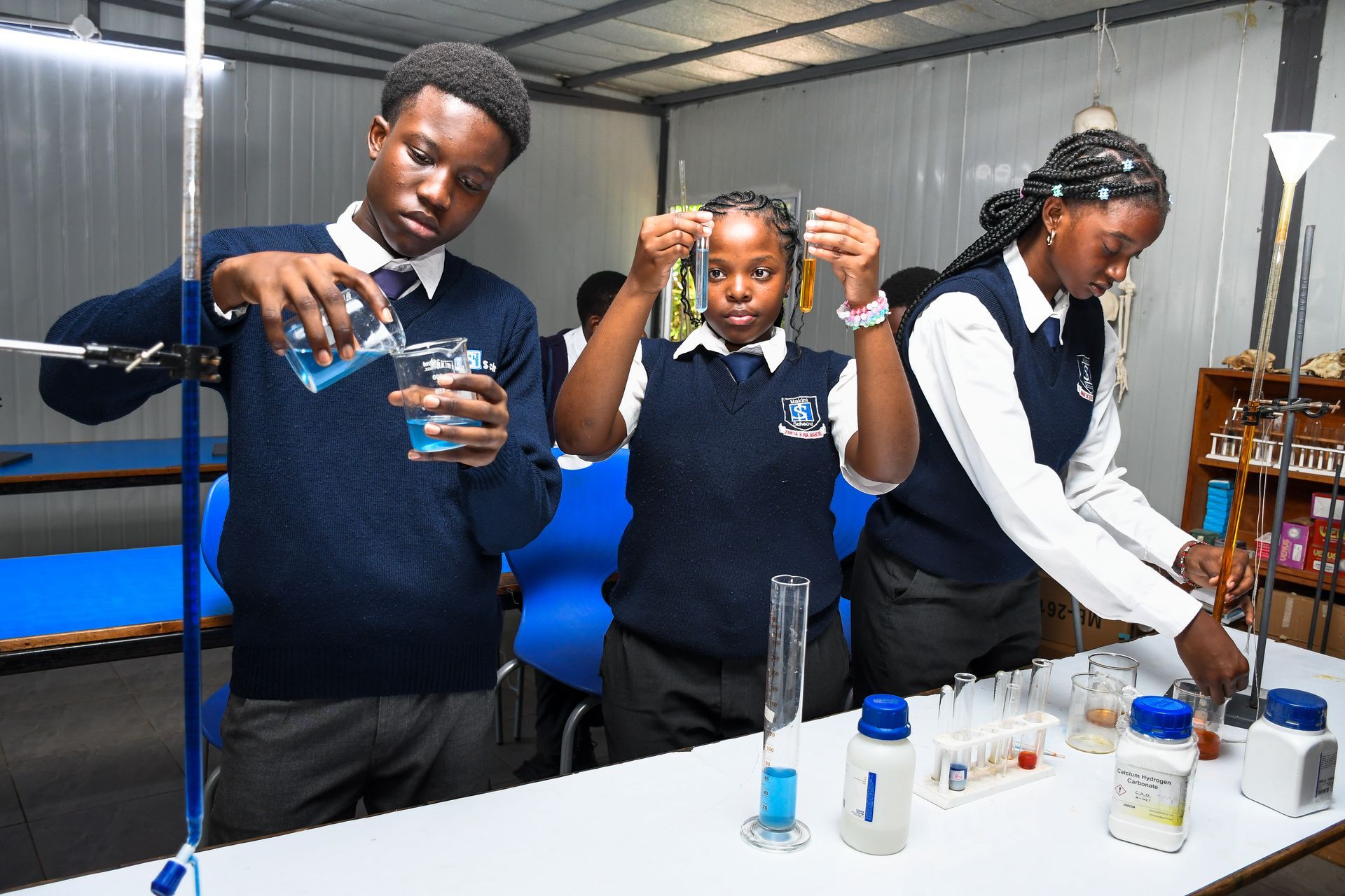 A man is standing next to a group of children sitting at desks in a classroom.