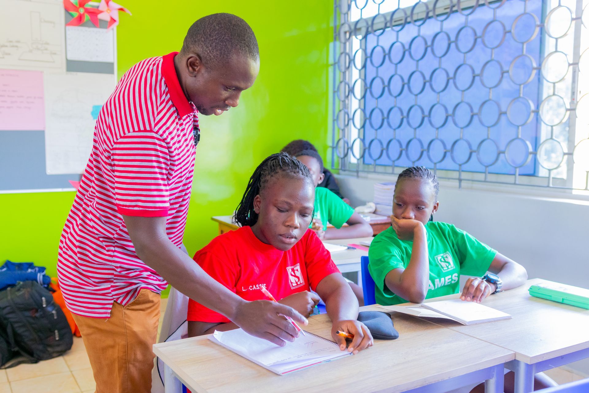 A man is standing next to a group of children sitting at desks in a classroom.