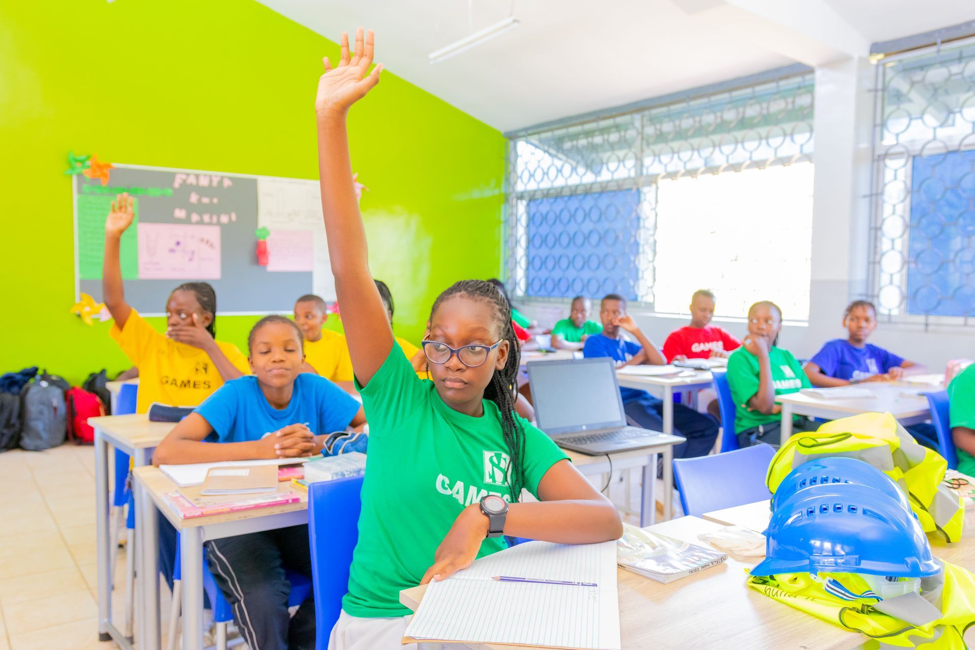 A group of children are raising their hands in a classroom.