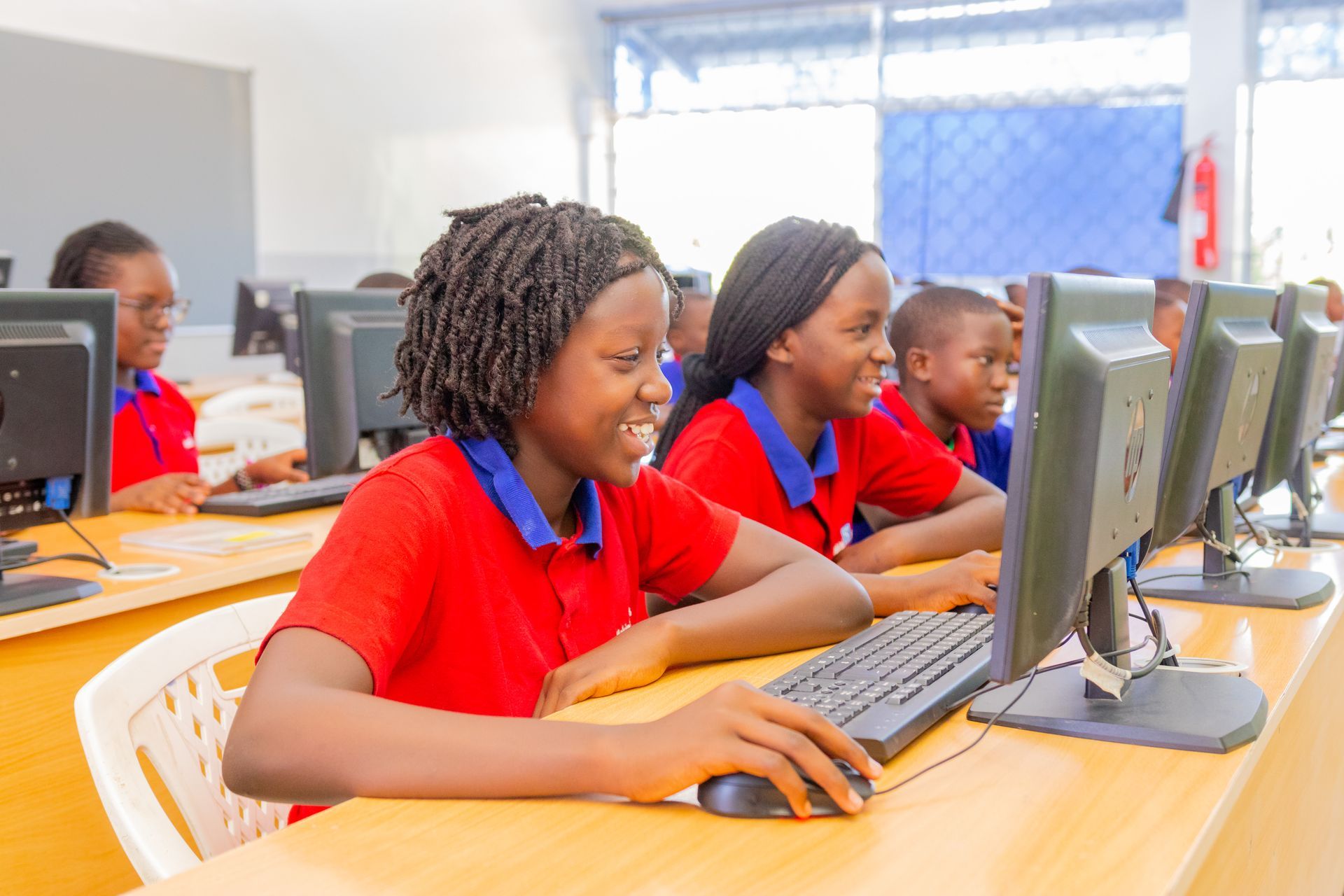 A group of children are sitting at desks in front of computer monitors.