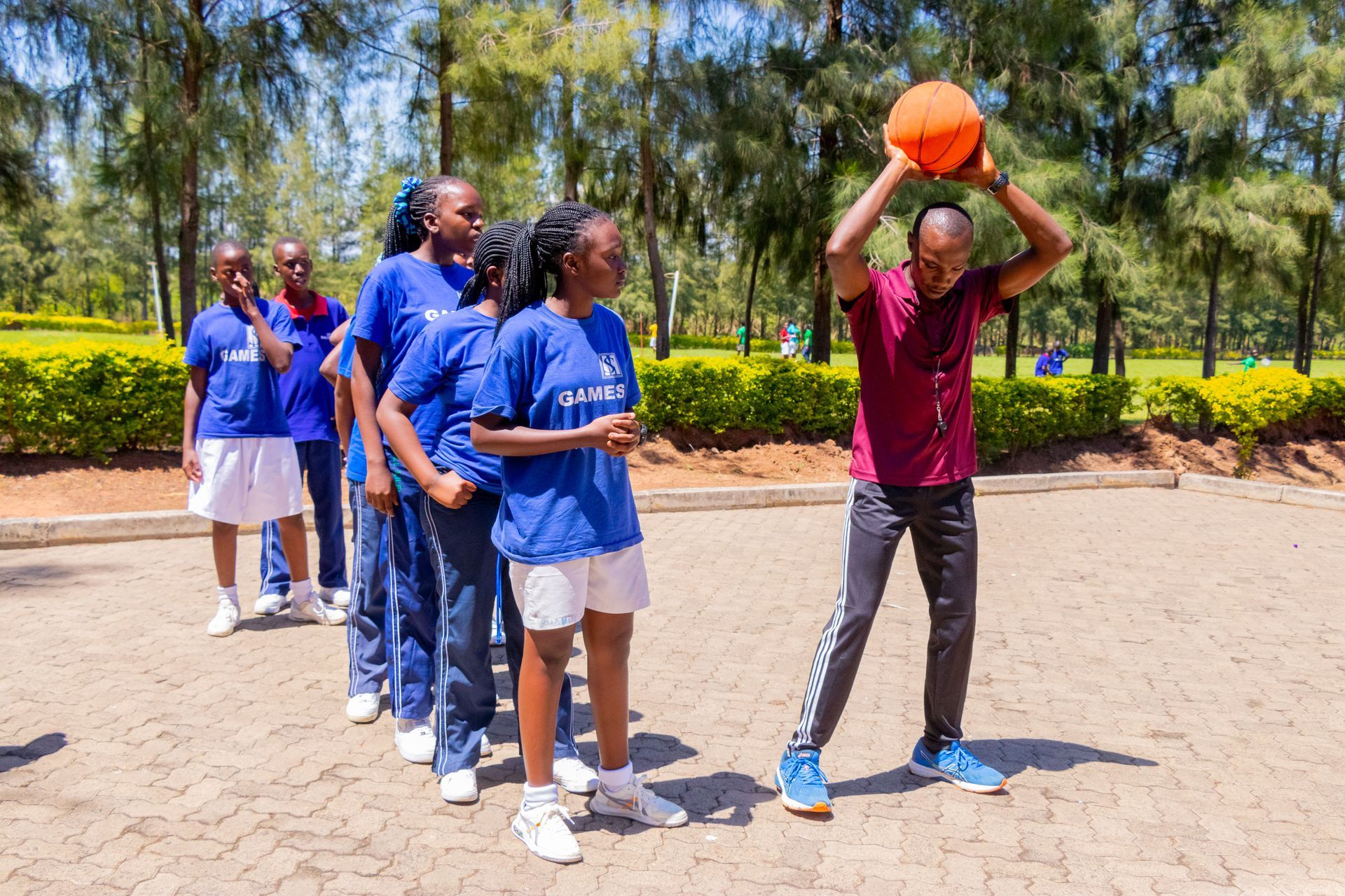 A man is holding a basketball over his head in front of a group of children.