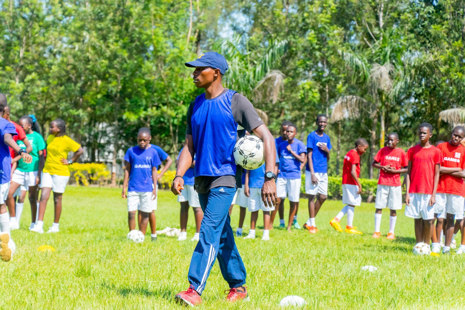 A man is holding a soccer ball in front of a group of children.