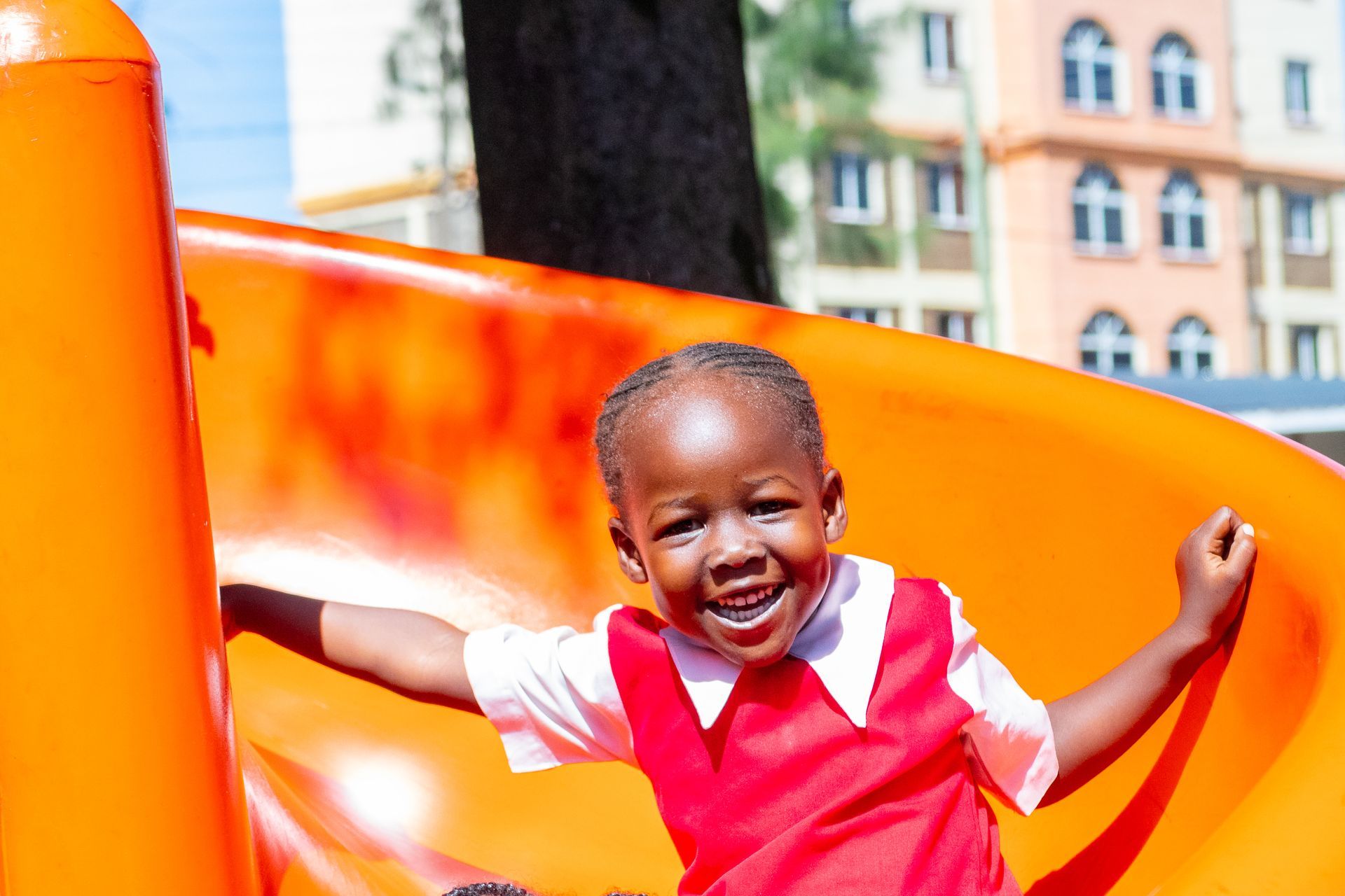 A little boy in a red dress is playing on an orange slide.