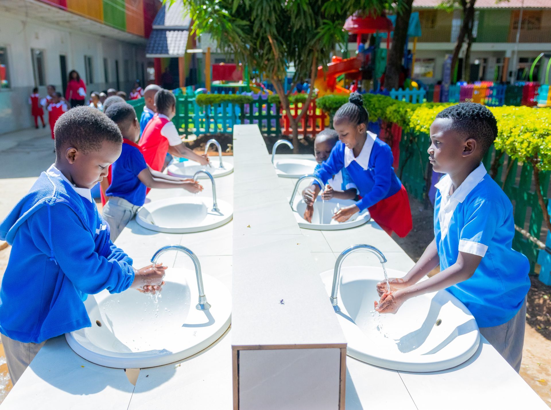 A group of children are washing their hands in a row of sinks.