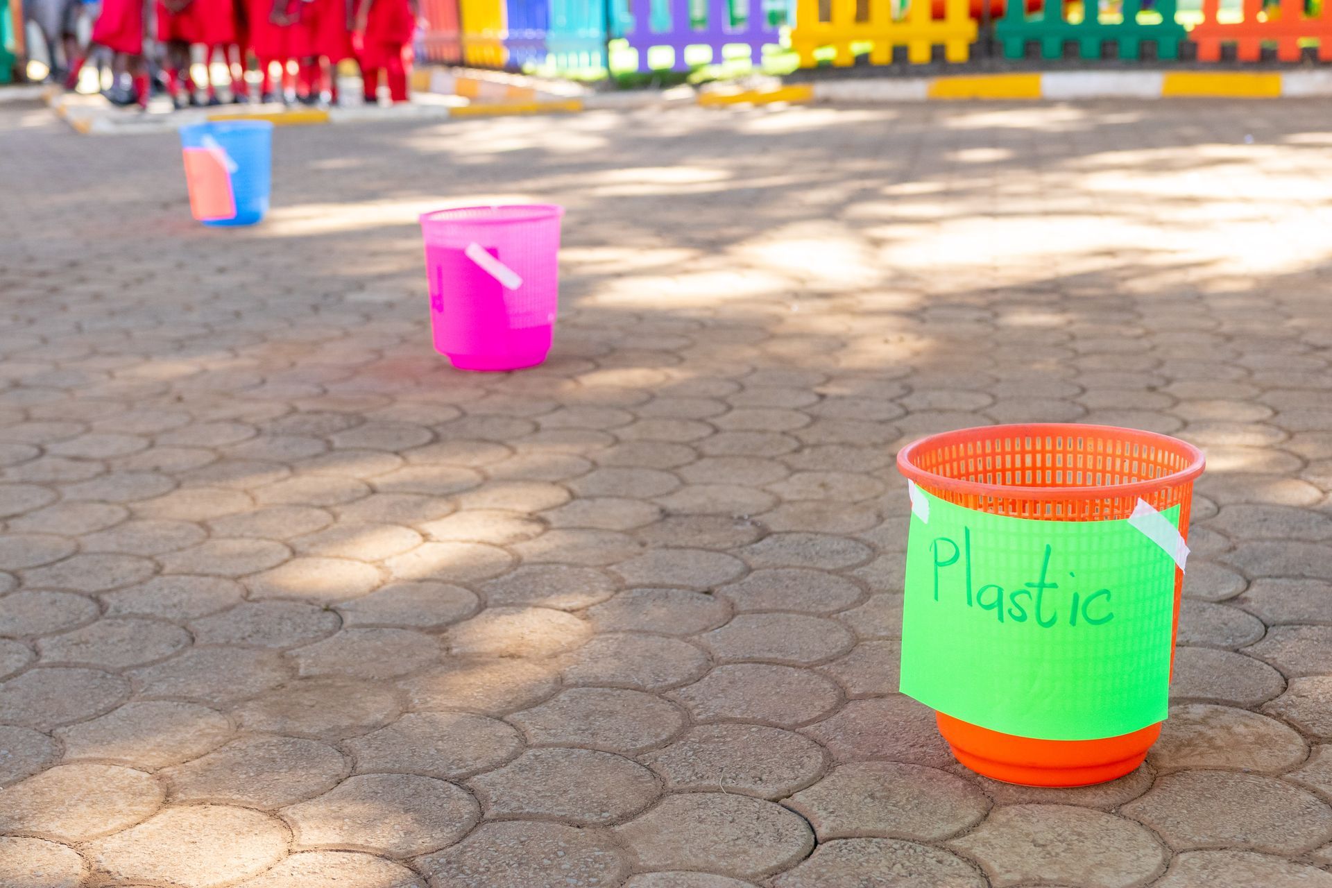 A green bucket with the word plastic written on it is sitting on a brick floor.