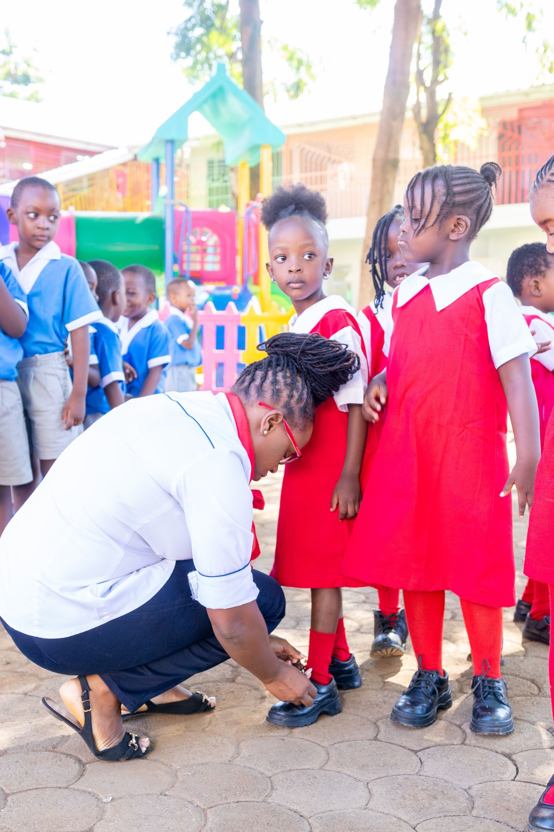 A woman is kneeling down next to a group of children in red uniforms.