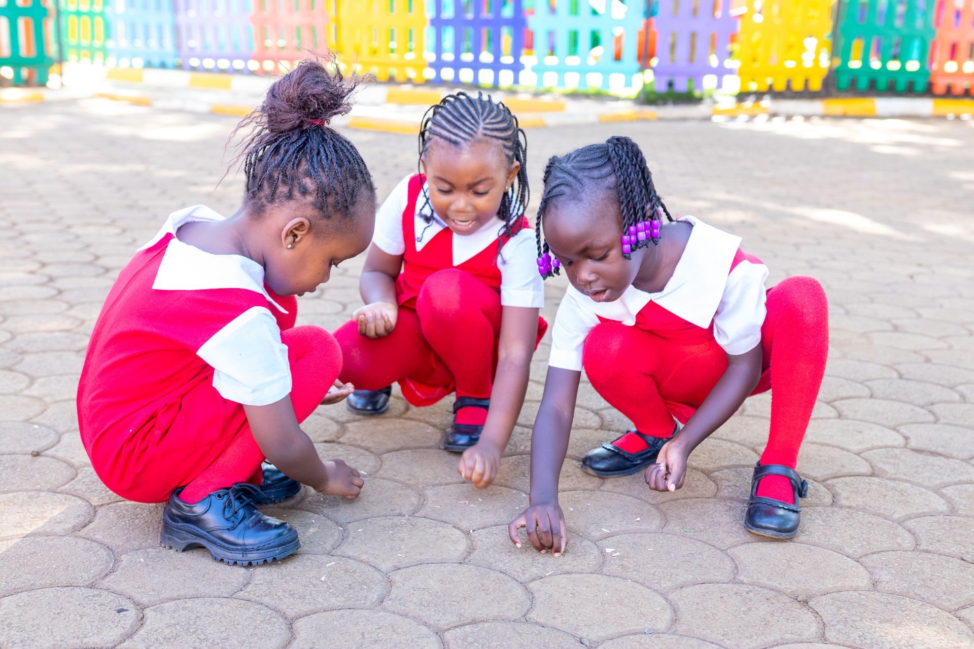 Three little girls are kneeling on the ground playing with marbles.
