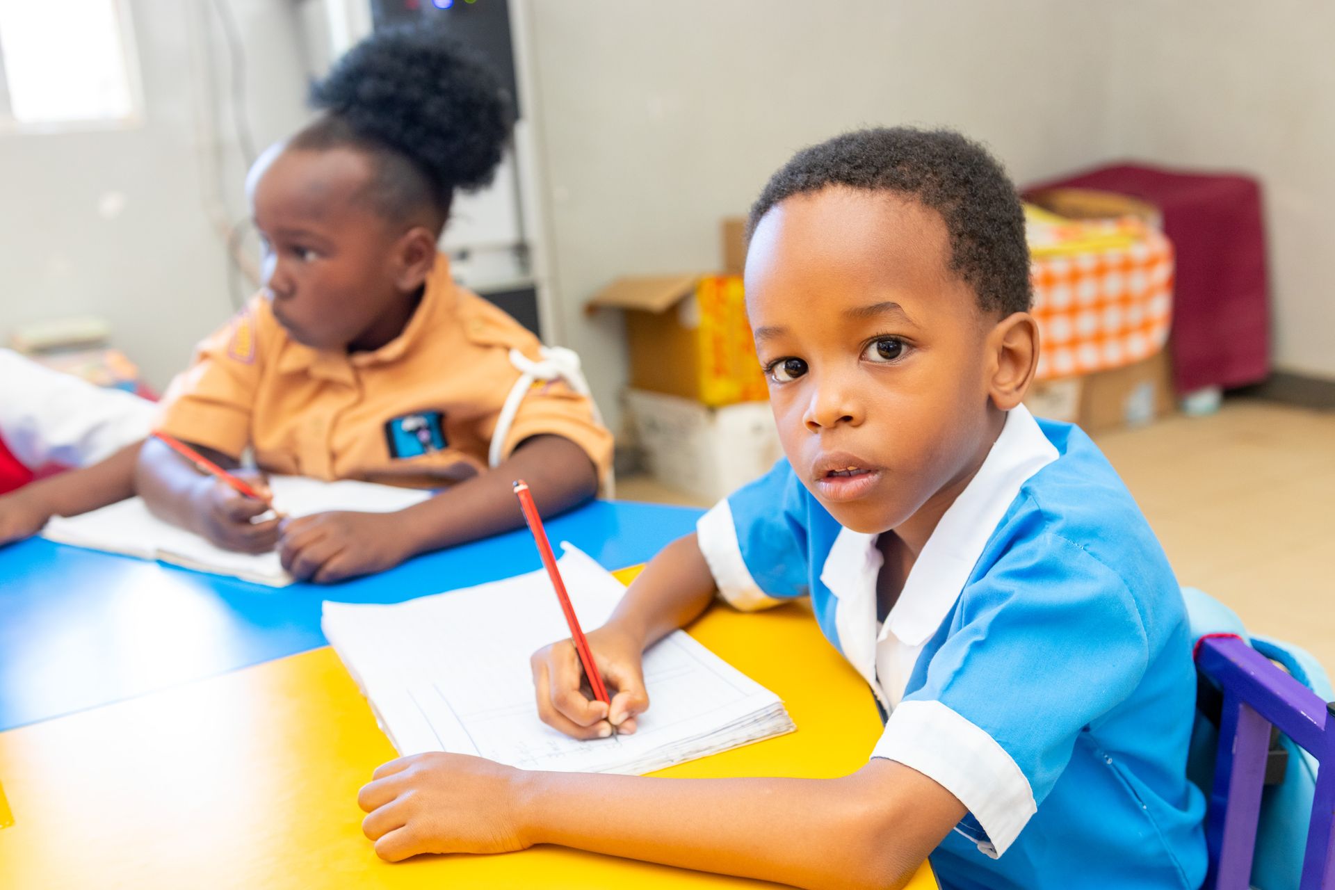 A boy and a girl are sitting at a table in a classroom writing in notebooks.