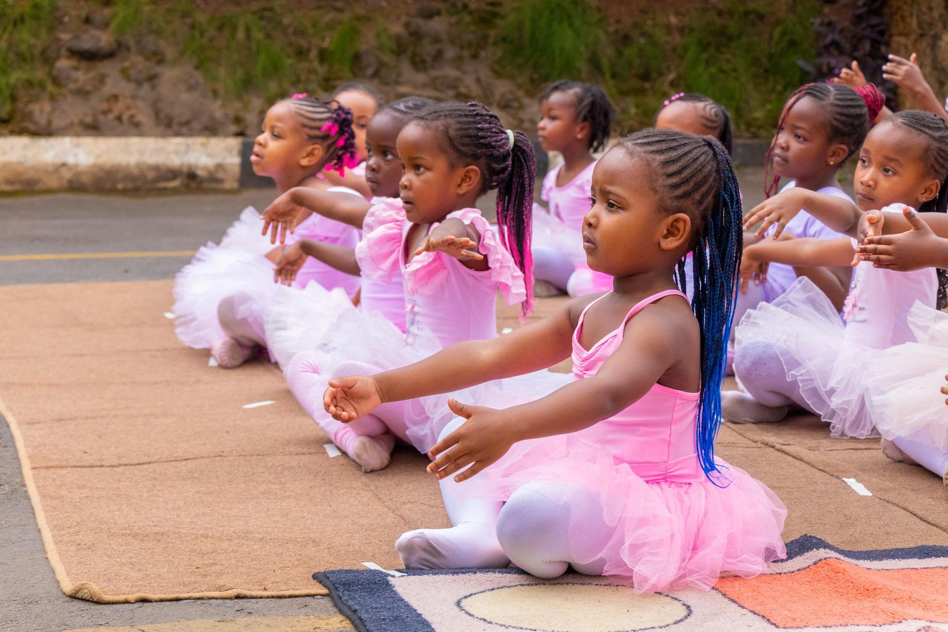 A group of little girls in pink tutus are sitting on the ground.