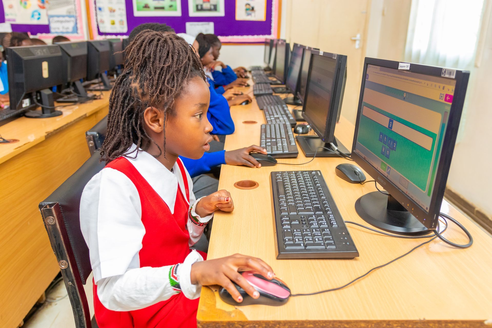 A girl is sitting at a desk in front of a computer in a computer lab.