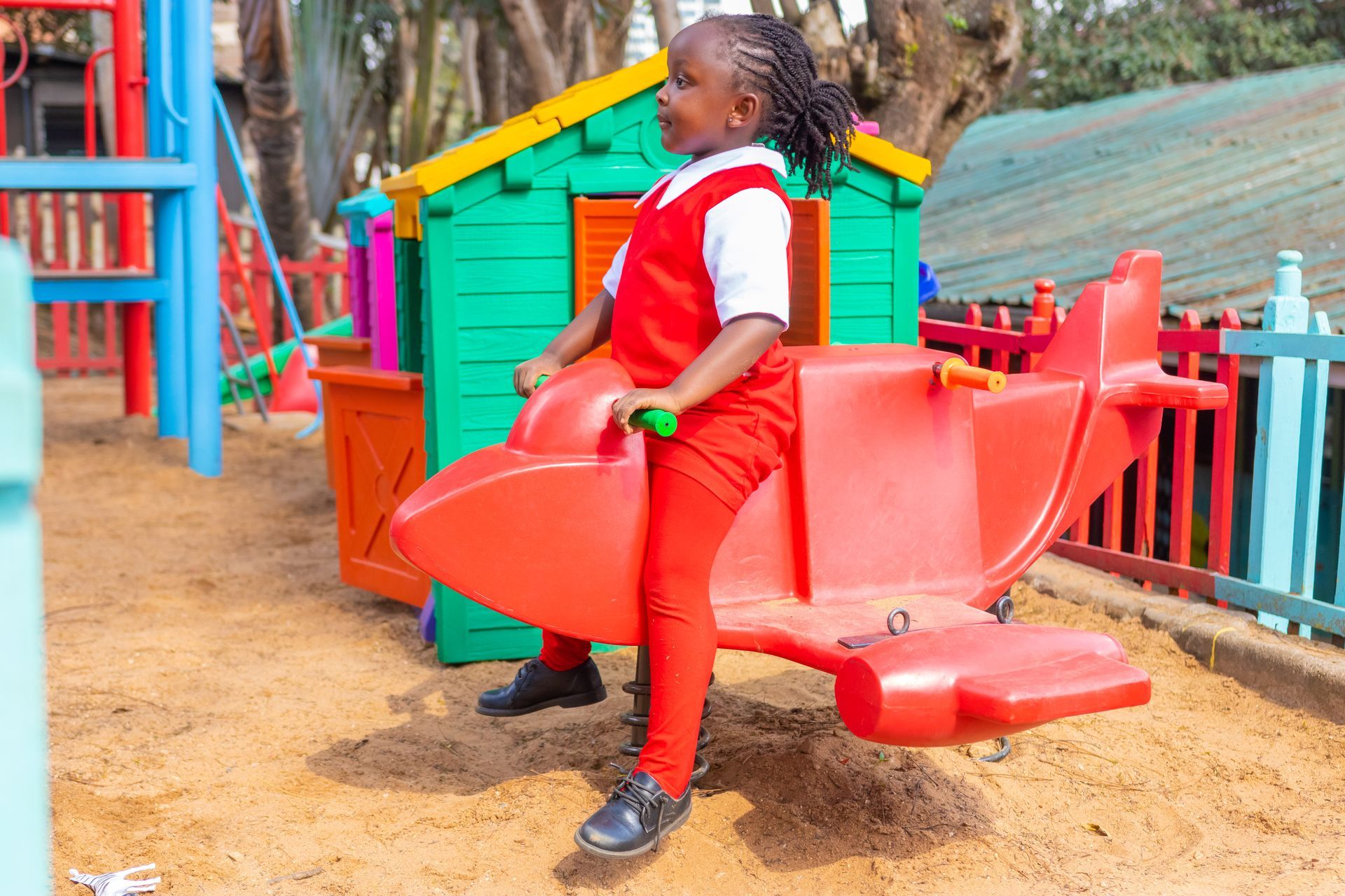 A little girl is sitting on a red airplane in a playground.