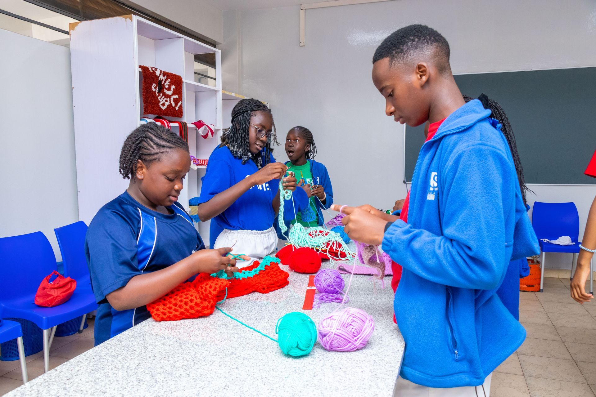 A group of children are knitting in a classroom.