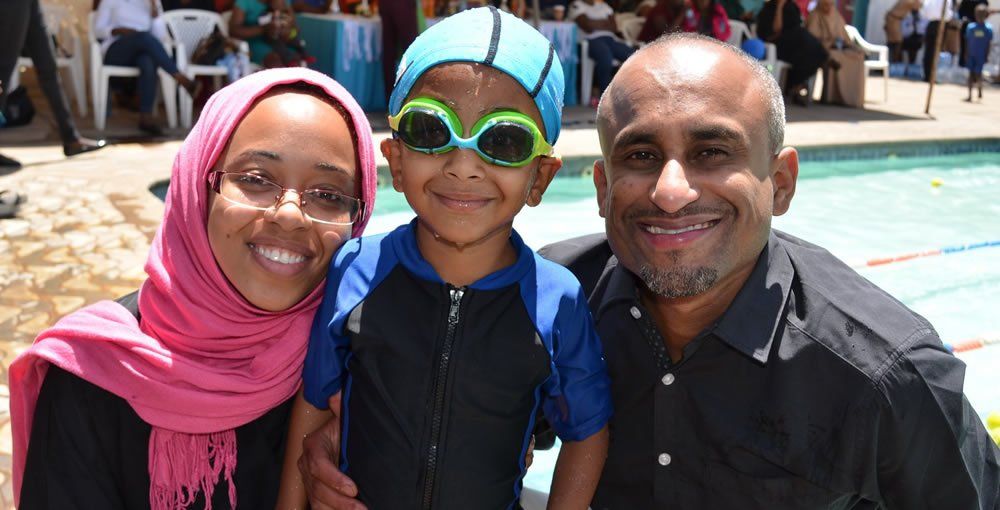 A man , woman and child are posing for a picture in front of a swimming pool.