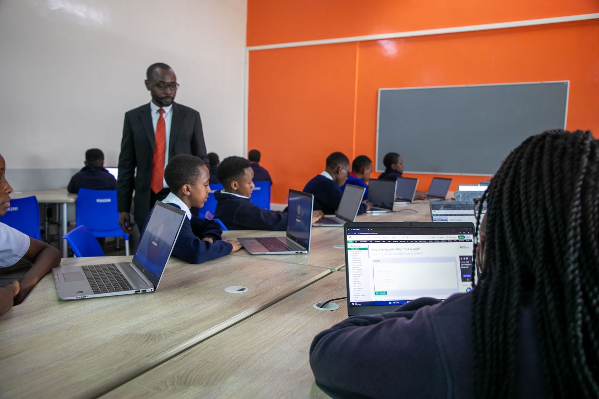 A group of children are sitting at tables with laptops in a classroom.