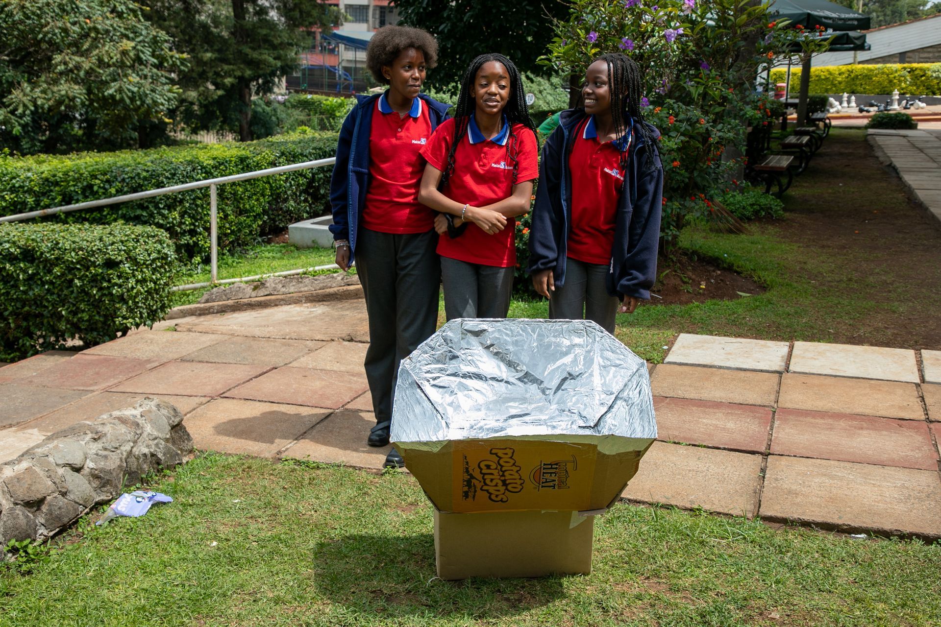Three girls are standing next to a cardboard box covered in aluminum foil.