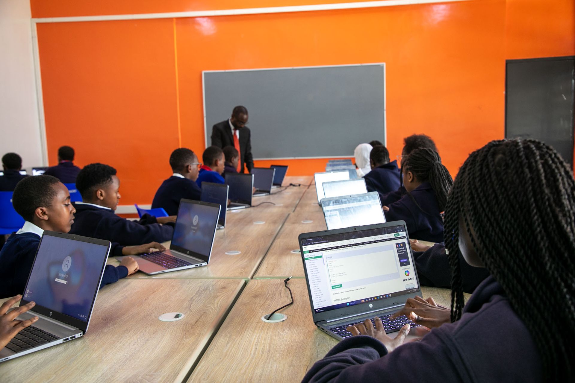 A group of children are sitting at tables with laptops in a classroom.