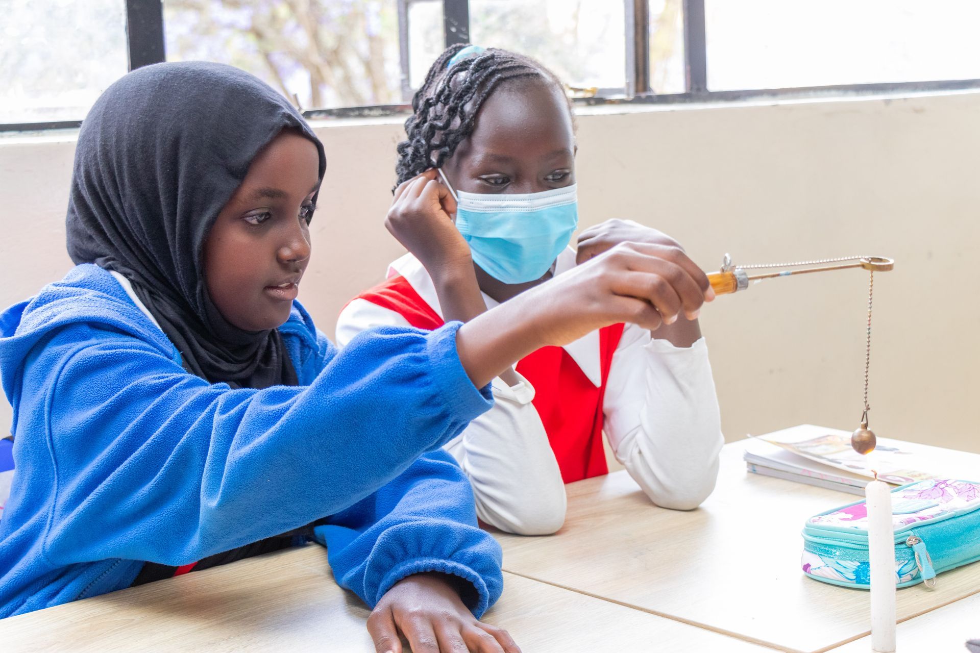 Two young girls wearing face masks are sitting at a desk in a classroom.