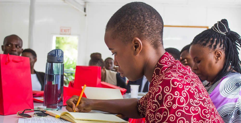 A young boy is sitting at a desk in a classroom writing in a notebook.