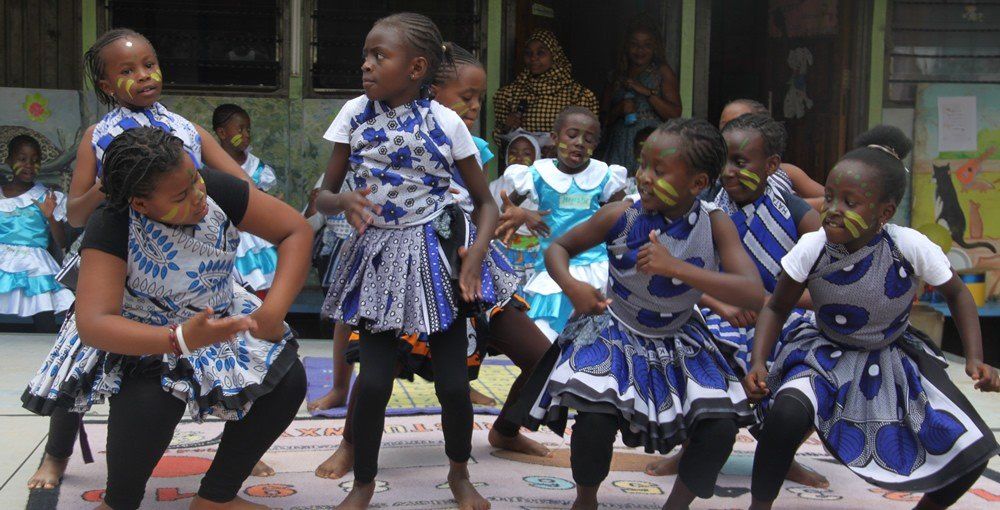 A group of children in blue and white dresses are dancing