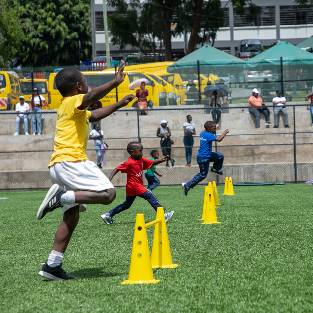 A boy in a yellow shirt is jumping over yellow cones