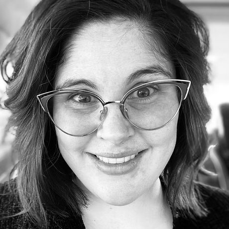 A woman wearing glasses is smiling in a black and white photo.