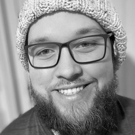 A man with a beard is wearing a beanie and smiling in a black and white photo.