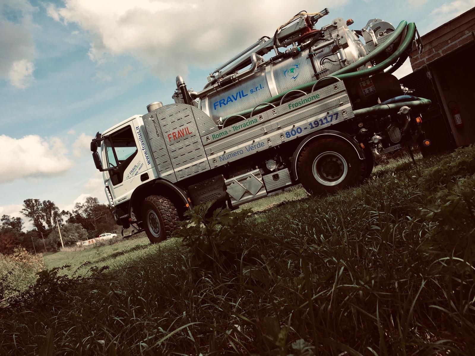 Un camion per la pulizia delle fosse settiche parcheggiato su un campo erboso sotto un cielo nuvoloso.