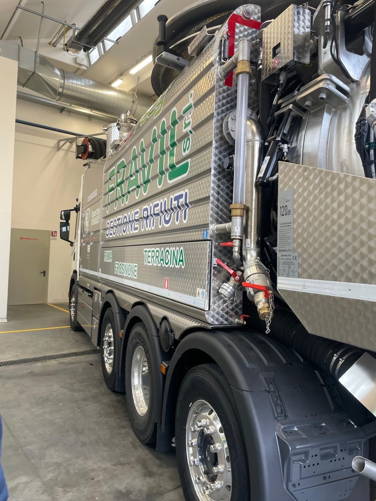 Un idraulico con tuta e guanti rossi ripara i tubi vicino a una caldaia a parete.