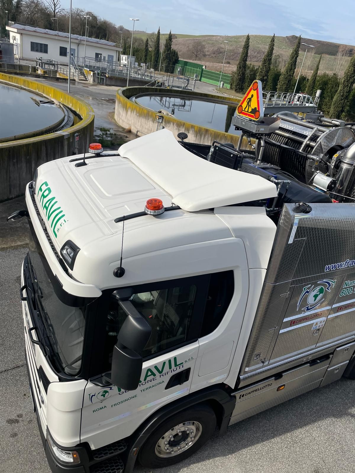 Un camion per la pulizia delle fosse settiche parcheggiato su un campo erboso sotto un cielo nuvoloso.