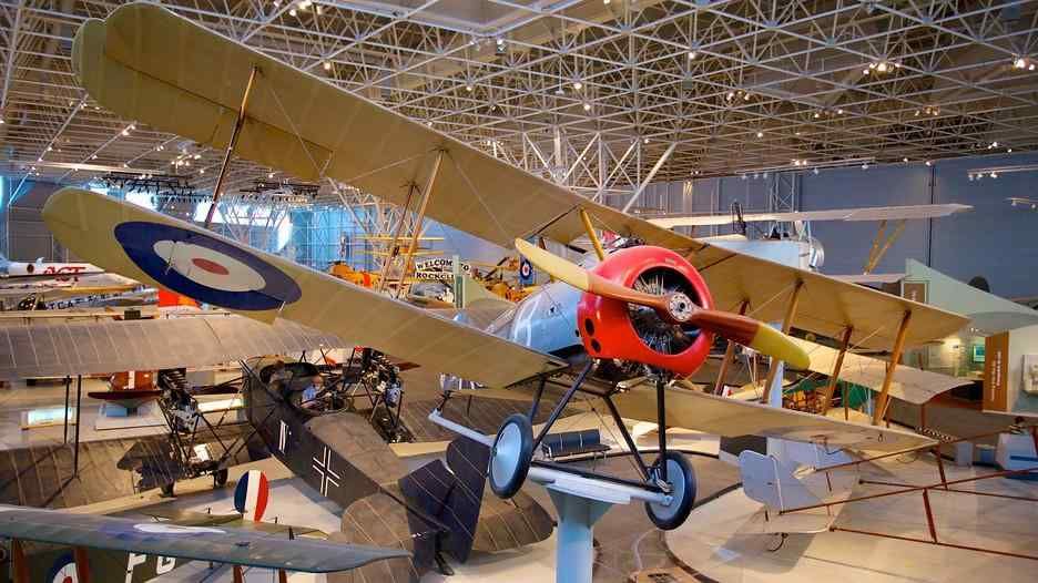 Vintage biplane suspended in a museum, with tan wings, red nose, and blue-white roundels.