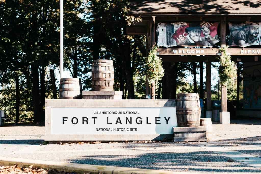 Fort Langley entrance sign with stacked barrels and trees in the background