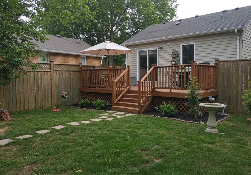Wooden deck with steps leading to a grassy backyard, surrounded by a wooden fence and a small birdbath.